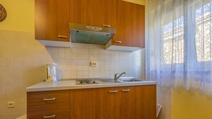 Une cuisine de taille réduite, dotée de meubles en bois, d’une hotte de cuisine en acier inoxydable et d’une fenêtre agrémentée de rideaux décoratifs.