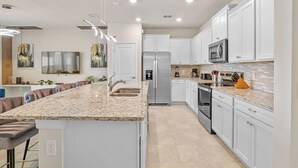 A modern kitchen with white cabinets, granite countertops, stainless steel appliances, and pendant lighting.