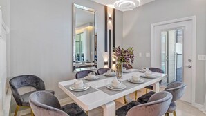 A dining area with a white table set for four, grey upholstered chairs, a vase with flowers, and a large mirror on the wall.