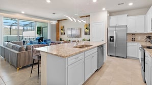 A modern kitchen with white cabinets, a stainless steel refrigerator, and a large island with a sink.