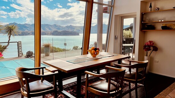 A dining area with a table and chairs, a vase with flowers, and a view of a lake and mountains.