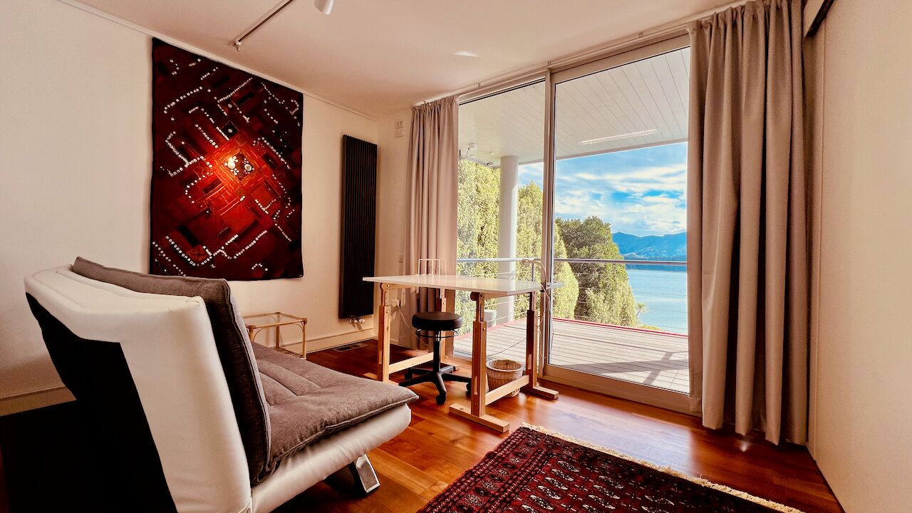 A modern room with a sofa, a small table, and a large window offering a view of the sea.