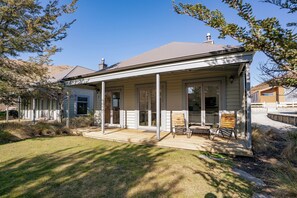 A single-story house with a covered porch, a sliding glass door, and a small outdoor seating area with two chairs and a table. - Gold Rush Chalet - Cardrona Holiday Home (Cardrona)