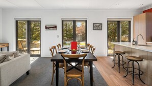 A modern kitchen with a dining area, featuring a large table, chairs, and a bar area with stools. - Gold Rush Chalet - Cardrona Holiday Home (Cardrona)