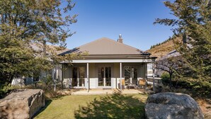 A single-story house with a covered porch, large rocks in the front yard, and a clear blue sky. - Gold Rush Chalet - Cardrona Holiday Home (Cardrona)