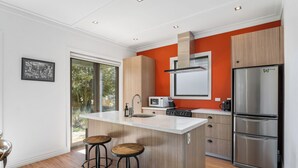 A modern kitchen with a central island, wooden cabinets, a stainless steel refrigerator, and a window overlooking greenery. - Gold Rush Chalet - Cardrona Holiday Home (Cardrona)