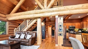 A log cabin interior with a leather sofa, wooden staircase, and a kitchen area. - Beautiful 5 bdrm lakefront log cabin - under 1hr from Mpls! (Maple Lake)