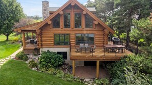 A log cabin with a deck, large windows, and a stone chimney. - Beautiful 5 bdrm lakefront log cabin - under 1hr from Mpls! (Maple Lake)