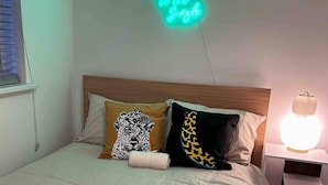A bed with a neon sign, pillows, and a bedside lamp. - London Flat Next to Central Line Tube Station (London)