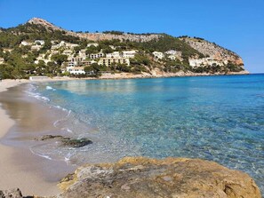Paesaggio costiero con acque limpide, una spiaggia sabbiosa e edifici su una collina.