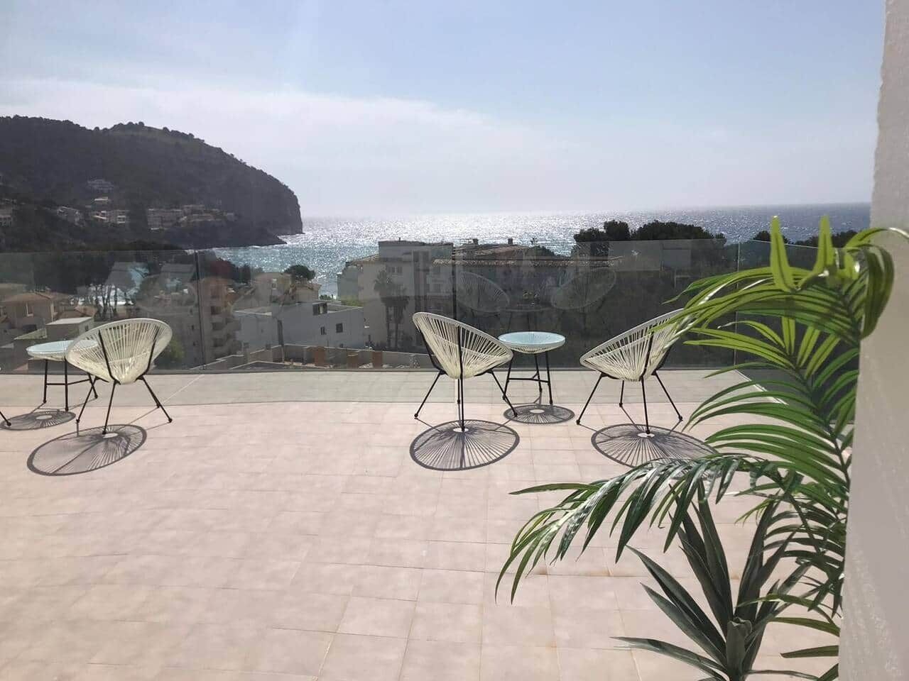 An outdoor terrace with chairs and tables, overlooking a coastal area with buildings and a hill.