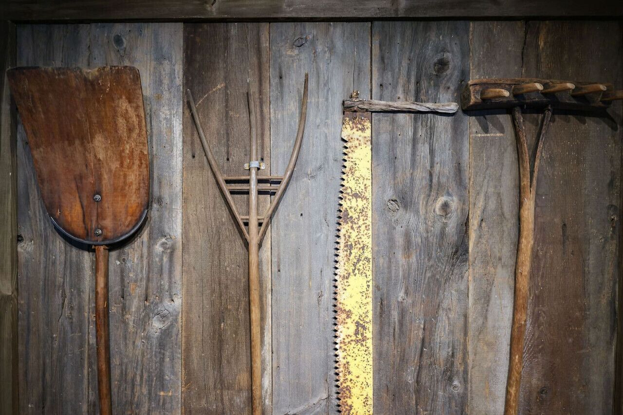 A wooden wall with three tools: a shovel, a pitchfork, and a saw.