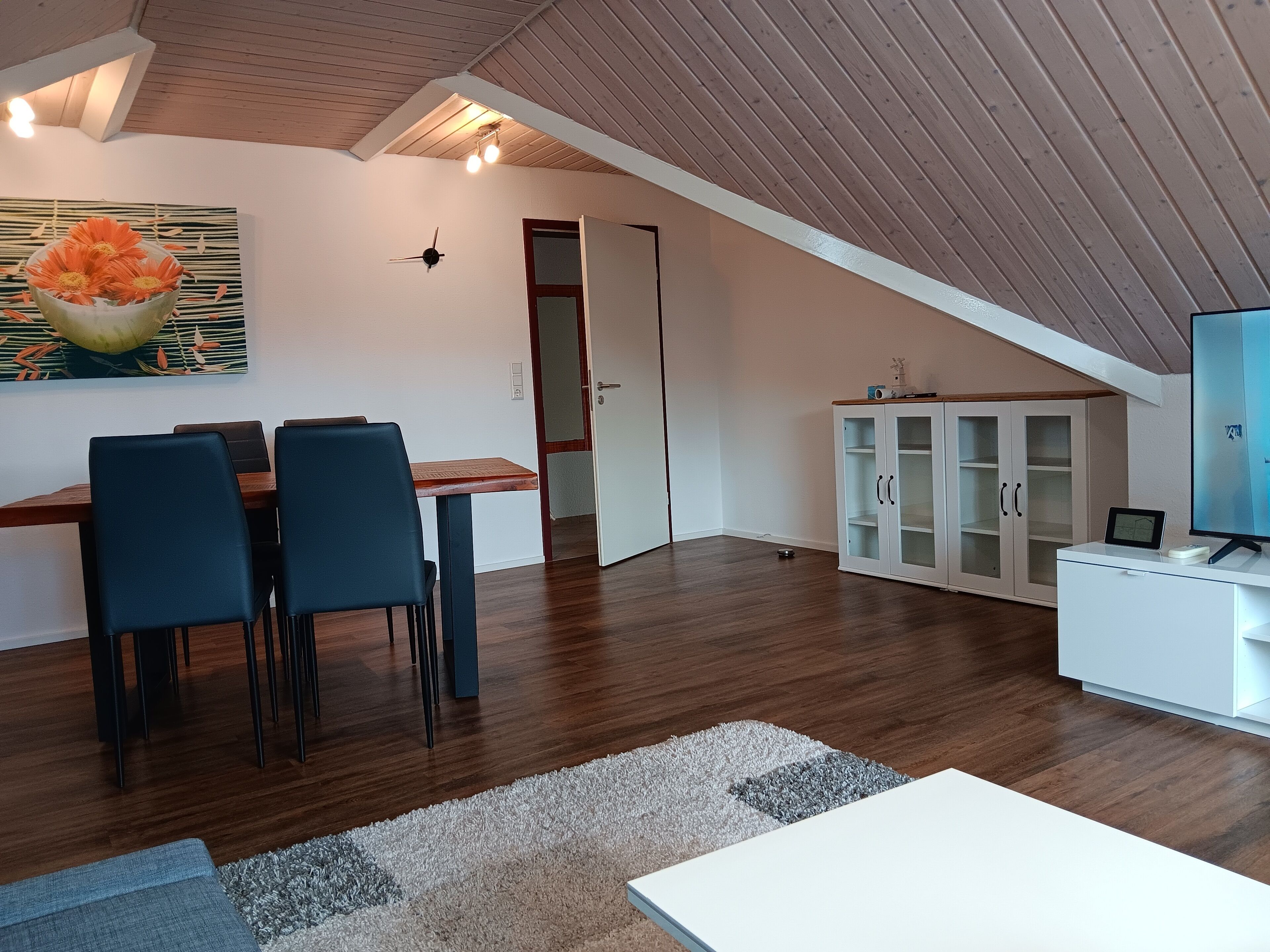 A modern loft apartment with a dining area, a TV, and a cabinet.