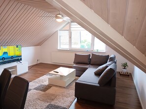 Un dormitorio estilo loft moderno con techo inclinado, un ventanal grande, un sofá, una mesa de centro y un televisor.