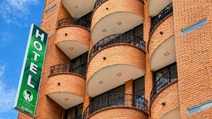 Um hotel com fachada de tijolos, várias varandas com grades de ferro forjado e uma placa verde indicando o nome e localização.