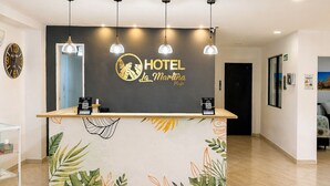 Balcão de recepção de hotel com um desenho de folha tropical, um relógio e uma placa com a inscrição 'HOTEL La Martina Playa'.
