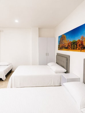 A hotel room with two beds, a wardrobe, a nightstand, and a painting of autumn trees.