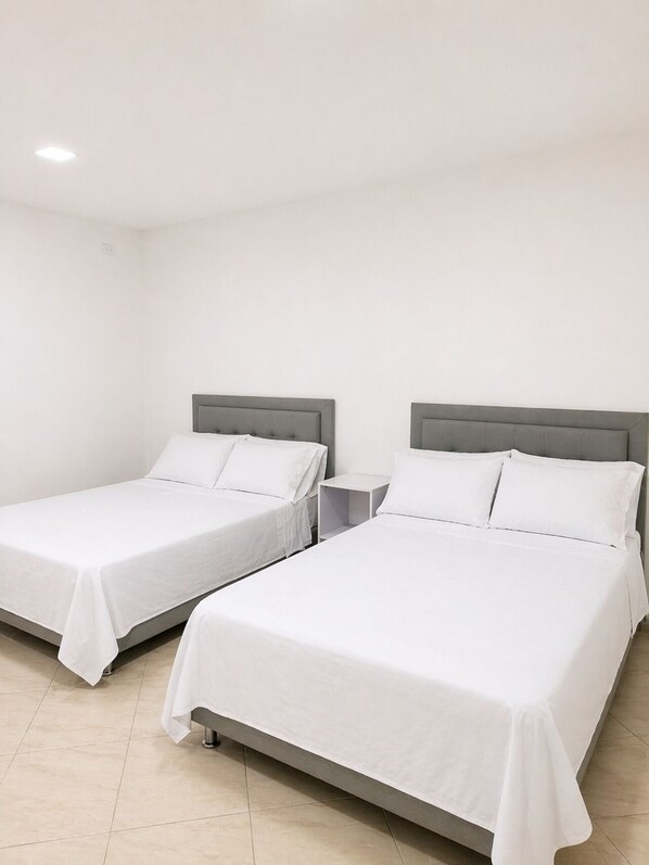 Two single beds with grey headboards and white bedding in a room with white walls and tiled flooring. - Hotel La Martina - Apartadó Antioquia (Apartadó)