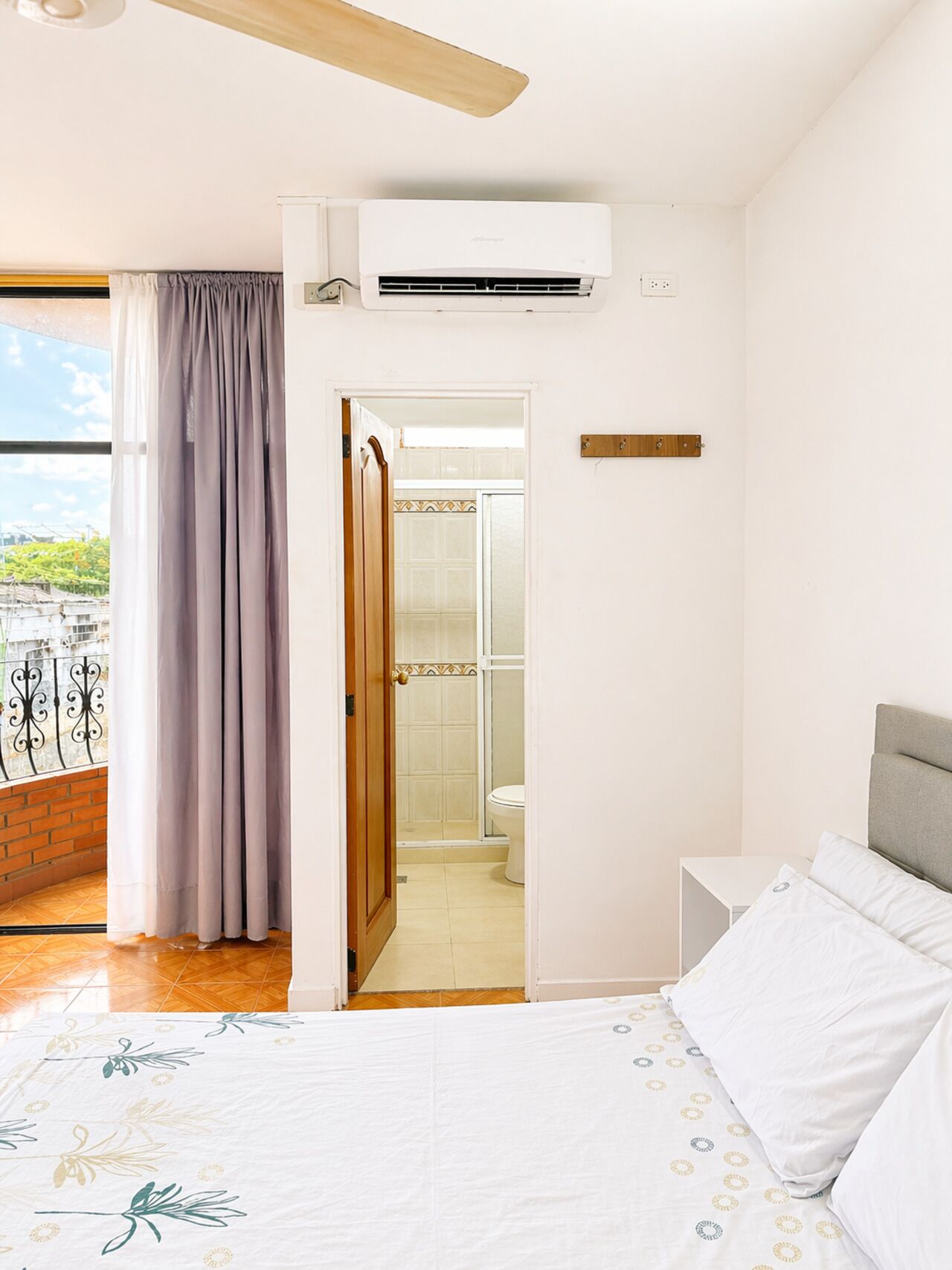 Un dormitorio con cama, ventana con cortinas, unidad de aire acondicionado y vistas al exterior.