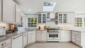 A modern kitchen with white cabinetry, a built-in oven, and a skylight. - Beachmore-Steps to Sandy Beach (Biddeford)