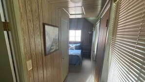 A hallway with wooden paneling, a framed picture, a bed with blue bedding, and a window with blinds. - Goldbug Hot Springs Getaway, Cozy Cabin Great for Hot Springs, Fishing & Hunting! (Salmon)