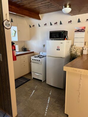 A compact kitchen with a gas stove, a microwave, and a refrigerator. There are decorative wall stickers of trees and animals. - Goldbug Hot Springs Getaway, Cozy Cabin Great for Hot Springs, Fishing & Hunting! (Salmon)