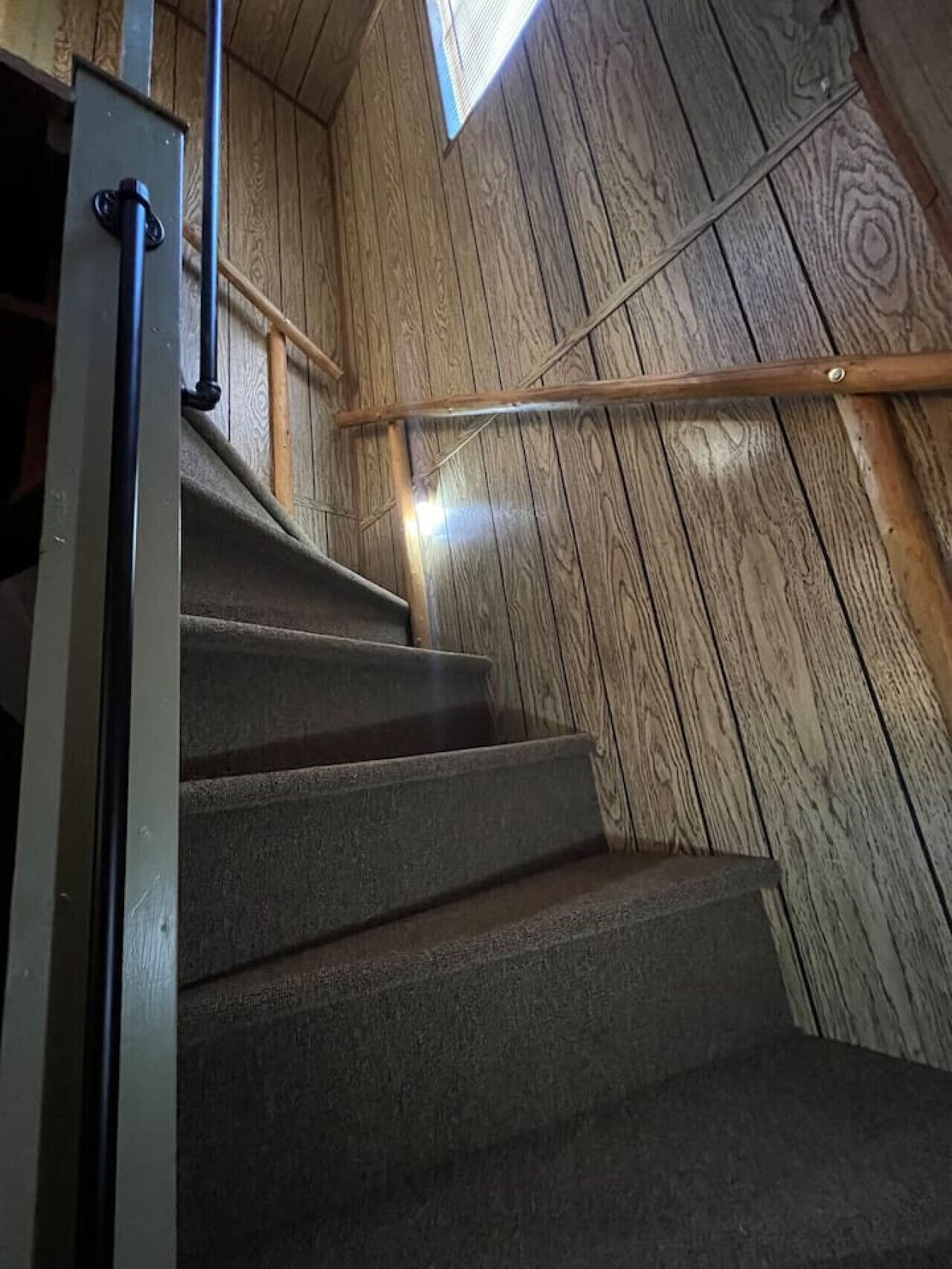 A wooden staircase with metal railings and a skylight above.