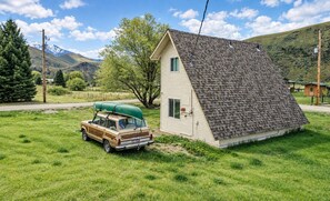 A house with a sloped roof, a parked car with a green cover, and a mountainous landscape in the background.