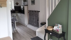 Cocina moderna con armarios blancos, microondas y cafetera. Hay un comedor con mesa y sillas, y una escalera con pared verde.
