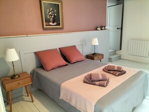 Une chambre à coucher avec un lit, deux tables de chevet, une lampe, un tableau encadré et un radiateur.