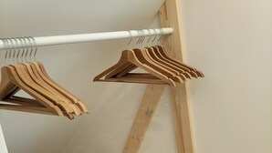 Un armario pequeño de madera blanca con un banco de madera y una barra metálica blanca para colgar ropa.