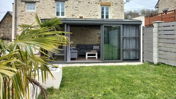 Una casa de piedra con una extensión moderna, que incluye un portal de cristal y un sofá gris.