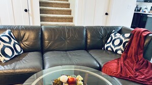 Un salon avec un canapé en cuir, une table basse en verre sur laquelle sont disposés des fruits, et un plaid rouge.