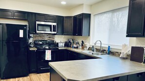 Une cuisine moderne avec des meubles de couleur sombre, un réfrigérateur en acier inoxydable, un four à micro-ondes, une cuisinière et un évier. On trouve deux tabourets en bois près de l’îlot central.