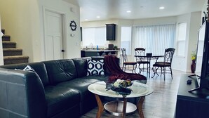 Un salon avec un canapé en cuir noir, une table basse sur laquelle sont disposés des fruits, et un coin repas avec une table et des chaises.