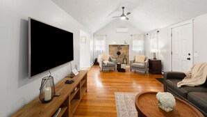 A living room with a flat-screen TV, wooden coffee table, two armchairs, a sofa, a fireplace, and a ceiling fan. - Peaceful Oasis minutes to T.F. Green International Airport, Main Street & more (East Greenwich)