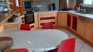 Una cucina funzionale con un tavolo rotondo e sedie rosse, dotata di microonde, forno e cappa aspirante in acciaio inossidabile.