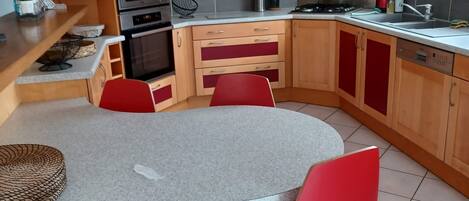 A compact kitchen with a round table and red chairs, equipped with a microwave, oven, and stainless steel range hood.