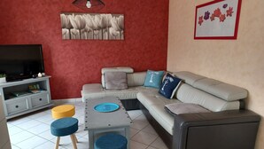 Un soggiorno con un divano, un tavolino, due poggiapiedi, una TV e un'opera d'arte a parete.
