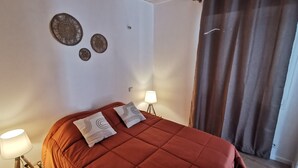 A bedroom with a red bedspread, two pillows, a bedside lamp, and wall art.