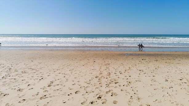 A beach with footprints leading to the water, a clear sky, and a calm sea.