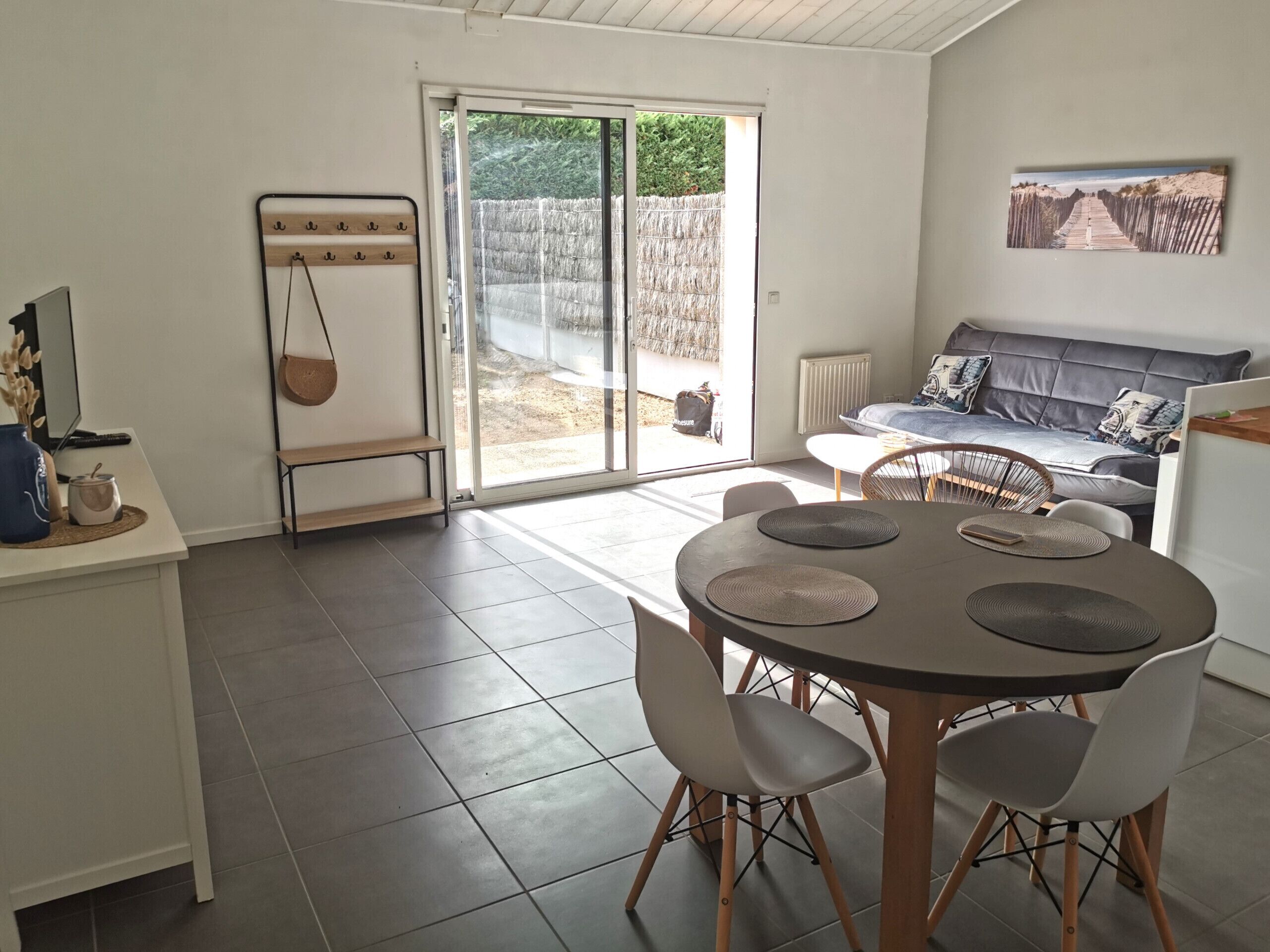 A modern living room with a sofa, a dining table with chairs, a coffee table, and a large window with a view of a garden.