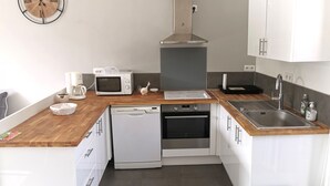 A modern kitchen with white cabinets, a wooden countertop, a microwave, a stove, a dishwasher, and a sink.