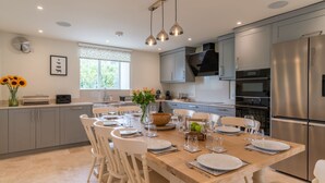 Een moderne keuken met grijze kastjes, een roestvrijstalen koelkast en een eethoek voor zes personen, compleet met witte stoelen en een houten tafel.