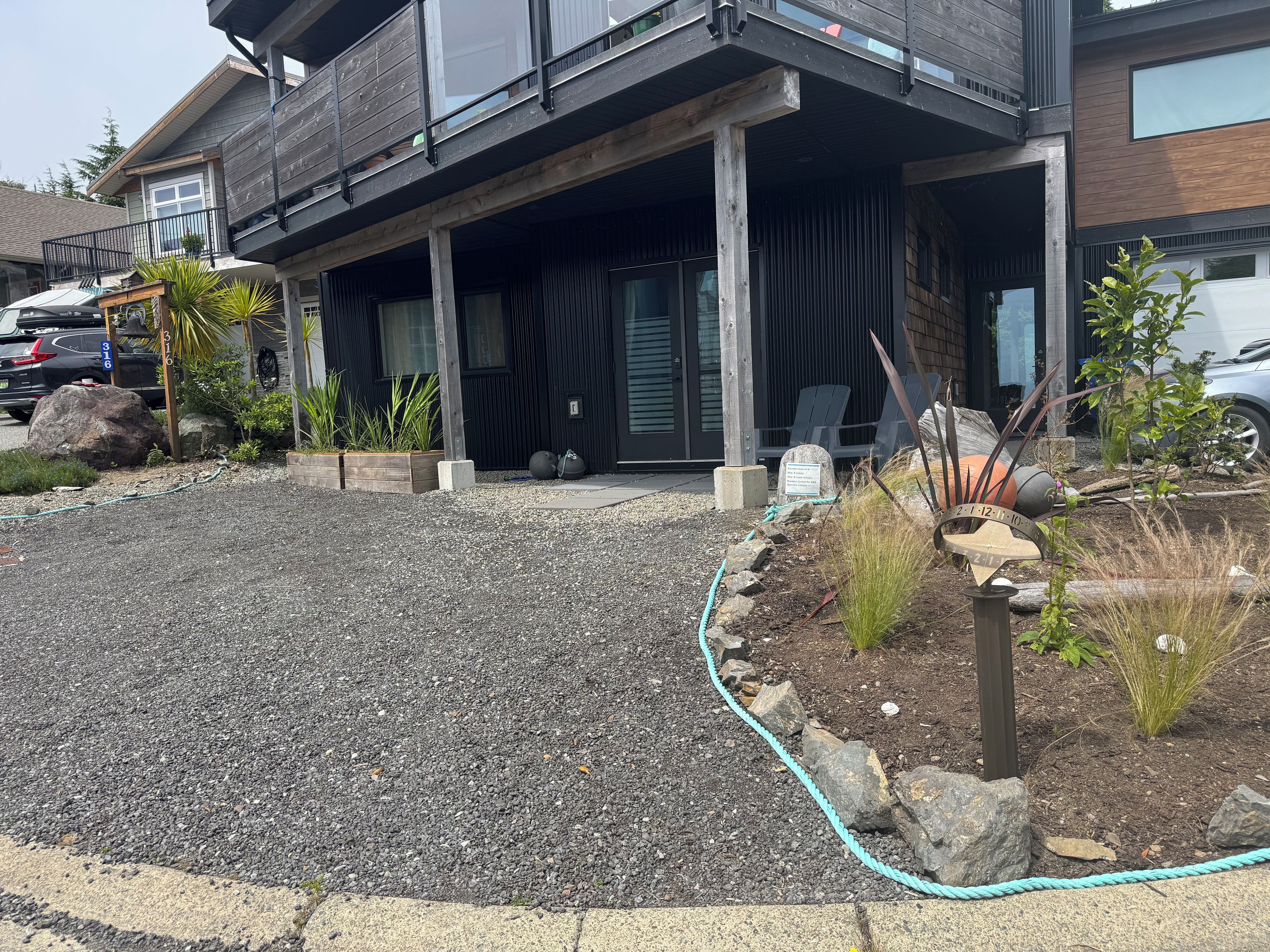 A modern building with a covered outdoor area, a gravel driveway, and a garden with plants and a rope border.