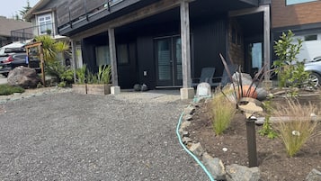 A modern building with a covered outdoor area, a gravel driveway, and a garden with plants and a rope border.
