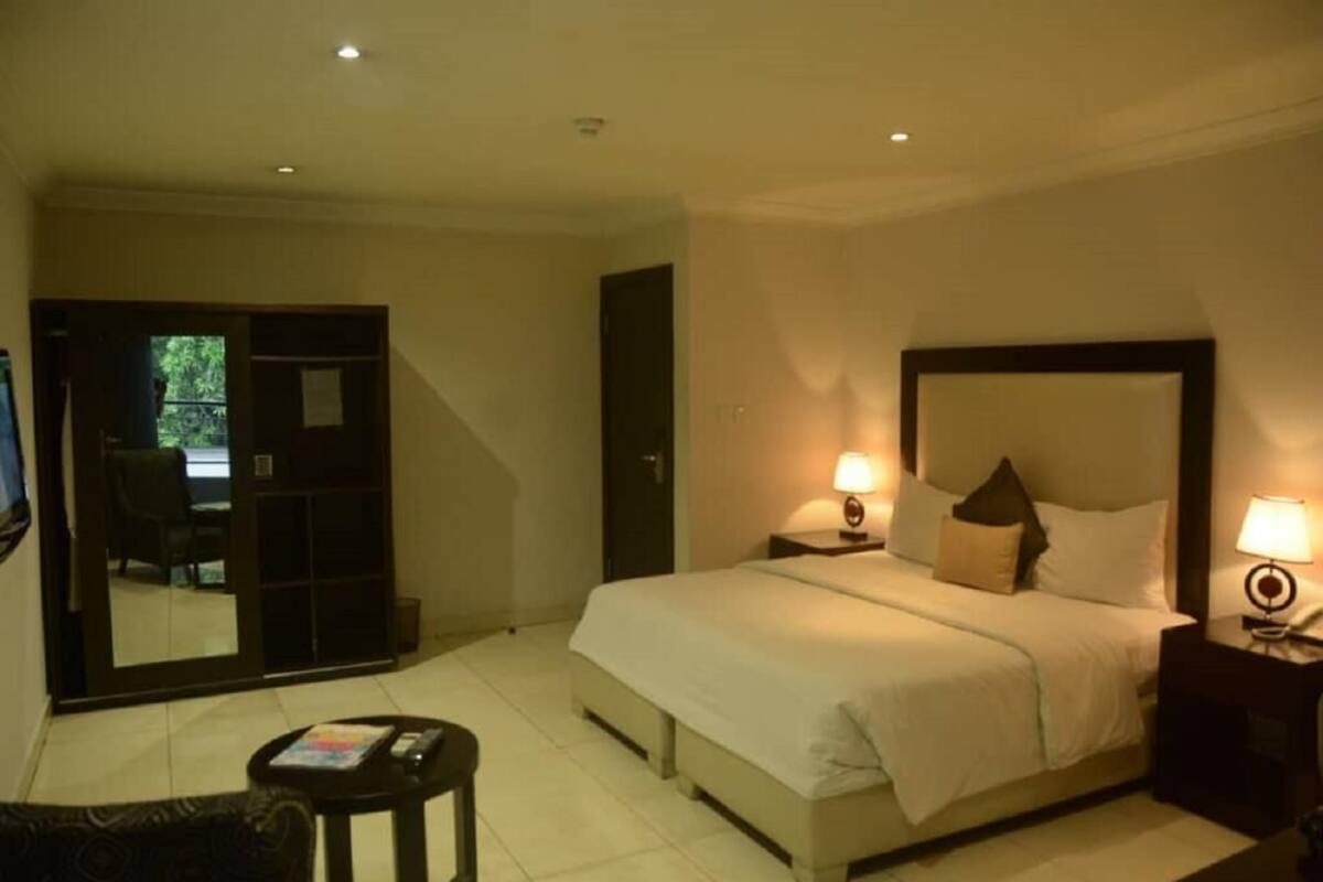 A hotel room with a bed, bedside lamps, a small table, and a chair.