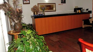 A reception area with a wooden reception desk, framed portraits on the wall, and a potted plant in the foreground. - Novel Suites And Resort (Jos)