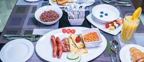 Une table dressée pour le petit-déjeuner, avec des assiettes de saucisses, de haricots, de pain grillé et un verre de jus d’orange.