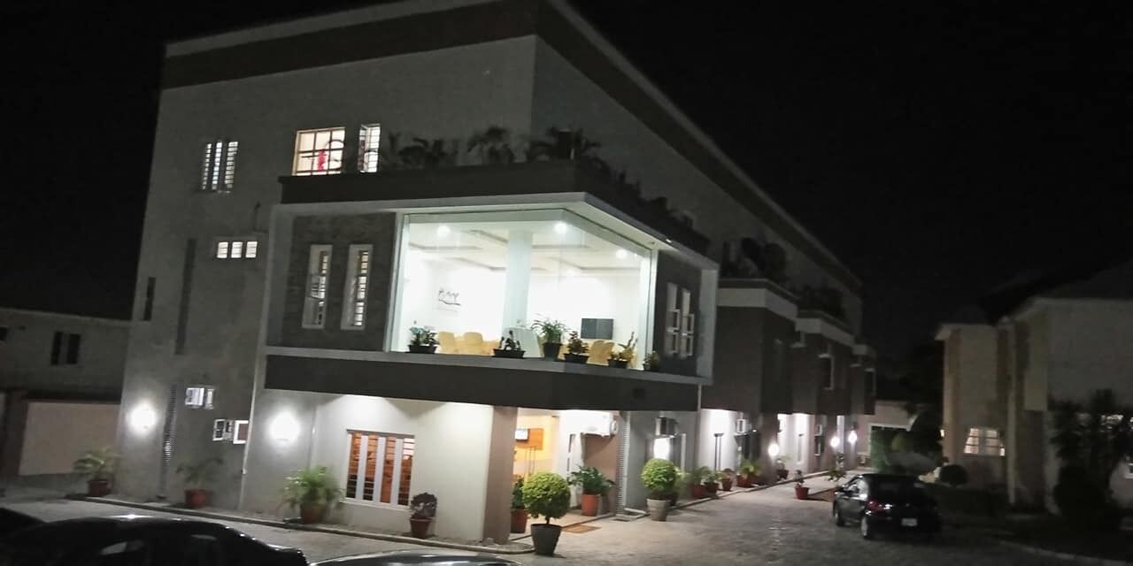 A two-story building with a balcony, potted plants, and a car parked in front.
